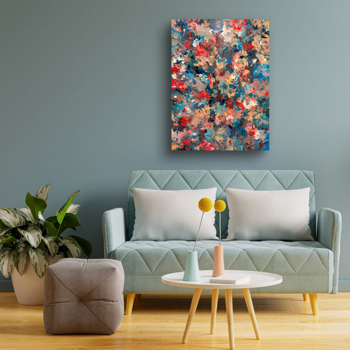 Bellissimo Processo hung on a soft blue grey wall above a mint green sofa with white cushions, a round white coffee table and a potted plant